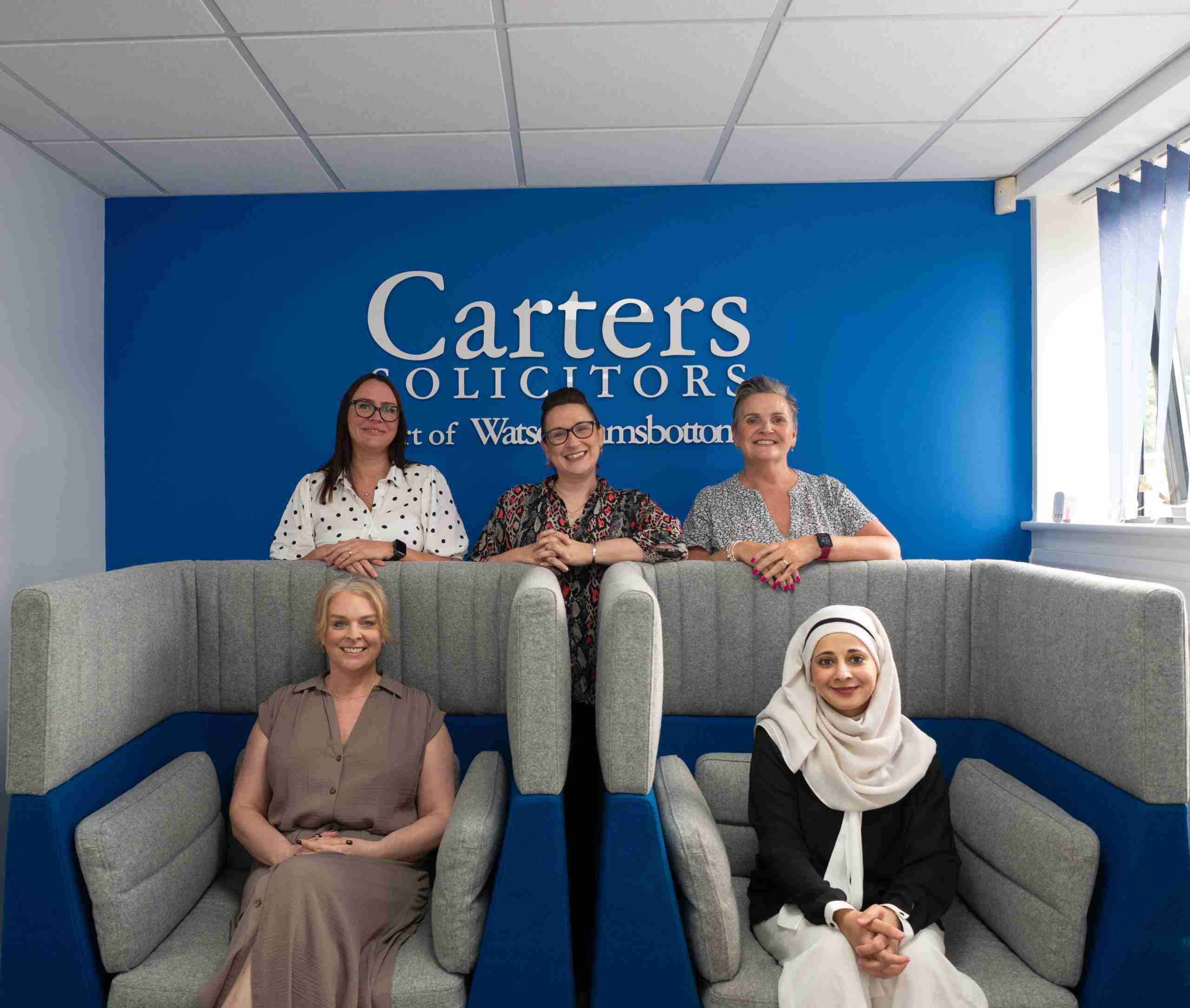 Delph office team photo in chairs with Carters logo wall sign behind